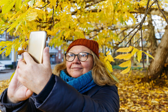 Senior woman taking selfie on smart phone in autumn park