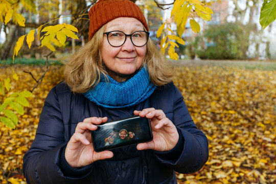 Happy senior woman showing screen of mobile phone with family picture in park