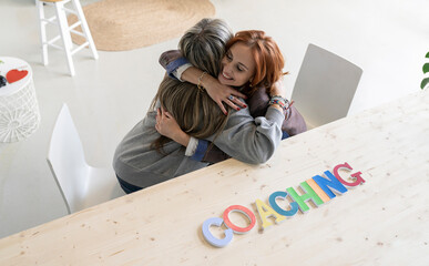 Coach embracing woman by desk at home office
