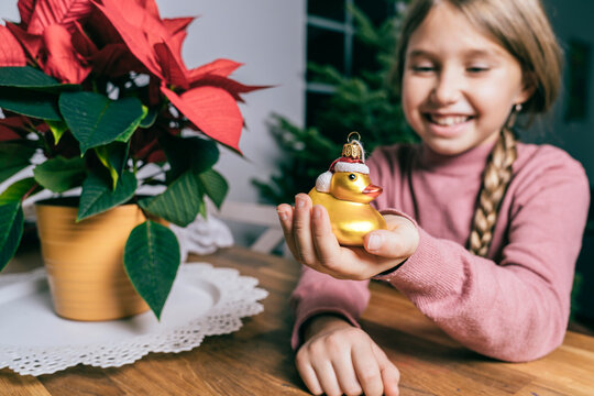 Smiling girl holding golden Christmas duck by star plant at home
