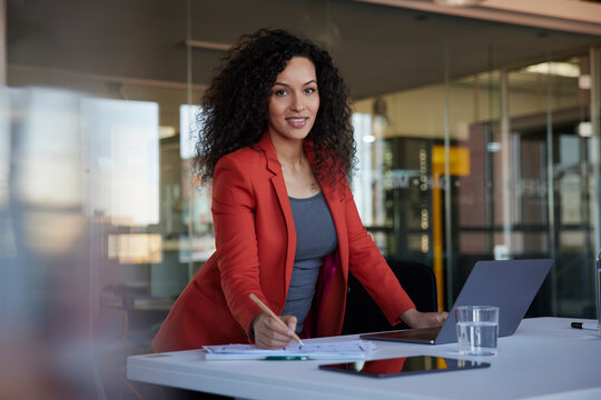 Smiling Businesswoman Writing On Paper Document On Desk In Office