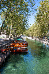 A tranquil scene with row of boats on a canal lined by trees on a summers day, in Annecy, France