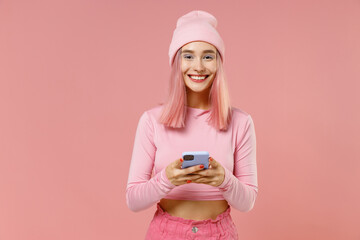 Young happy woman with bright dyed rose hair in rosy top shirt hat hold in hand use mobile cell...