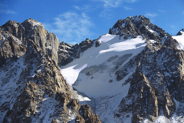Alpine rocky peaks of Tuyuk-Su with glacier and snow, beautiful gray rocks covered with snow, sky with small clouds, sunny