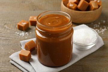 Yummy salted caramel in glass jar and candies on wooden table