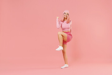 Obraz na płótnie Canvas Full body young woman 20s with bright dyed rose hair in rosy top shirt hat do winner gesture clench fist raise up leg isolated on plain light pastel pink background. People lifestyle fashion concept.