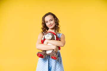 portrait of a beautiful girl in the studio. model in a blue dress with white polka dots plays with soft toys, has fun. yellow background. kindergarten teacher, nanny