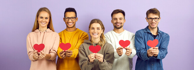 Studio group portrait of happy cheerful positive kind mixed race multiethnic young people who celebrate Valentine's Day holding red paper hearts and smiling isolated on purple color banner background - obrazy, fototapety, plakaty