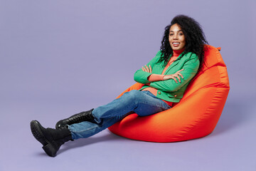 Full size body length bright fun young black curly woman 20s wear casual clothes sit in bag chair...
