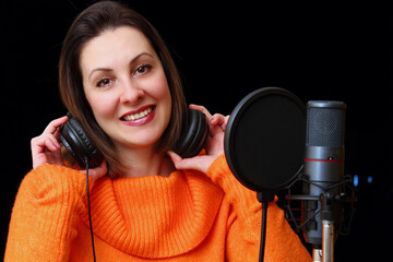Woman With Headphones And Studio Microphone ; Close up female vocalist in recording studio singing into microphone