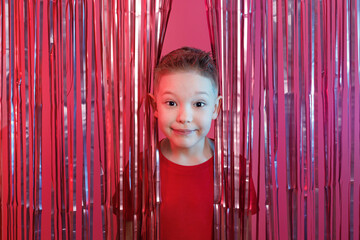 Little cute boy in a red T-shirt peeks out of a foil curtain. Children party.