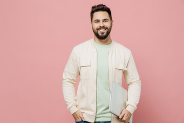 Young smiling happy cheerful caucasian man 20s wearing trendy jacket shirt hold use closed laptop pc computer isolated on plain pastel light pink background studio portrait. People lifestyle concept.