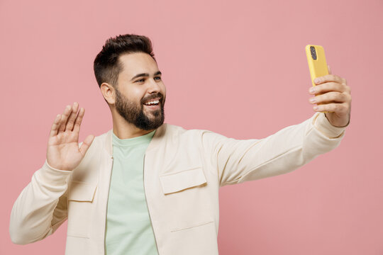 Young smiling caucasian fun happy man 20s in trendy jacket shirt doing selfie shot on mobile cell phone post photo on social network waving hand isolated on plain pastel light pink background studio