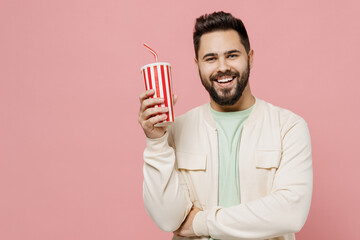 Young smiling cheerful fun happy caucasian man 20s wear trendy jacket shirt hold soda cola cup of fizzy water isolated on plain pastel light pink background studio portrait. People lifestyle concept.