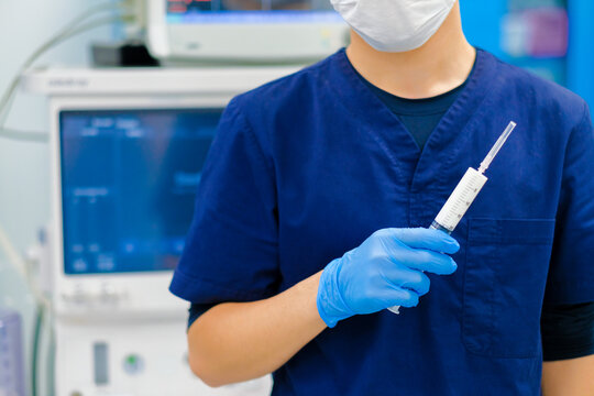 Selective focus on a large white syringe in the doctor's hand. The doctor's hand in a sterile glove holds a syringe. A doctor with a syringe against the background of modern medical equipment.