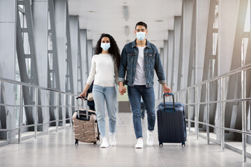 Travels During Pandemic. Arab Couple Wearing Masks Walking With Suitcases At Airport