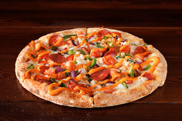 Pizza with pepperoni, tomatoes, peppers, onions and sauce lies on a wooden table made of boards. Angle view.
