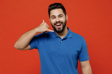 Young smiling happy caucasian man 20s wear basic blue t-shirt looking camera doing phone gesture like says call me bac isolated on plain orange background studio portrait. People lifestyle concept