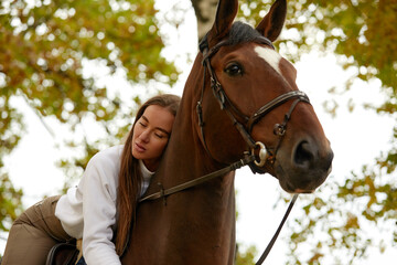 Fototapeta premium Beautiful brunette on a horse on the background of an autumn landscape. Horseback riding, active horseback riding