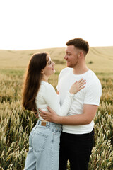 young couple in love stand in a wheat field at sunset of the day. guy with a girl on a romantic summer date. cute couple of lovers