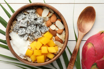 Bowl of granola with pitahaya, mango, almonds and yogurt on white wooden table, flat lay