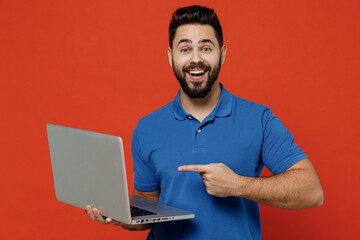 Young surprised happy man wear basic blue t-shirt hold use work on laptop pc computer browsing chatting surfing internet isolated on plain orange background studio portrait. People lifestyle concept.