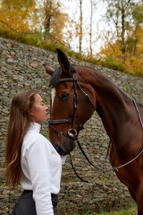 Fototapeta premium Beautiful young woman with horse outdoor. Concept of animal care. Rural rest and leisure. Idea of green tourism. Young european woman wearing helmet and uniform.