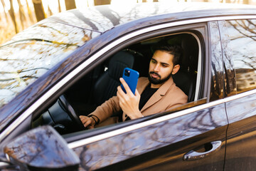 Driver taking photo with camera smartphone driving in car. Happy man taking picture with smart phone camera out window of car during travel road trip.