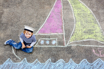 Little kid boy as pirate on ship or sailingboat picture painting with colorful chalks on asphalt....