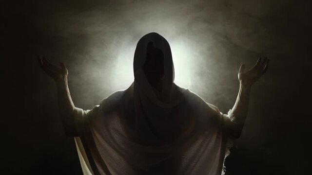 Holy man raises his hands against bright light