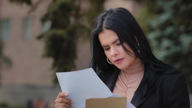 Close-up serious young woman sitting outdoors reading paper letter sad girl feels resentment upset about bad news find out about failed exams college dropout refusal notice financial difficulties