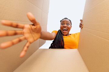 Bottom view of excited black woman receiving online order, unpacking her carton parcel at home
