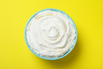 Bowl of tasty cream cheese on yellow background, top view