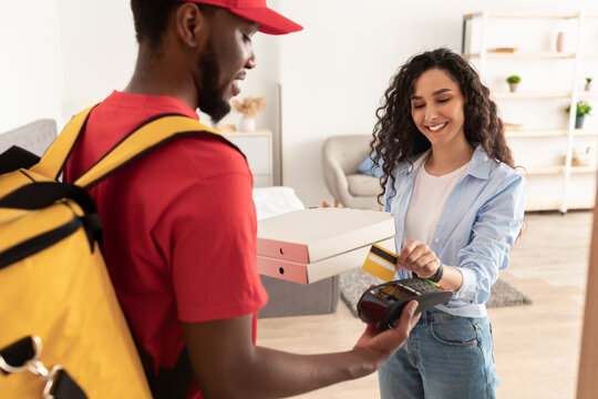 Smiling deliveryman holding POS machine, woman paying with card
