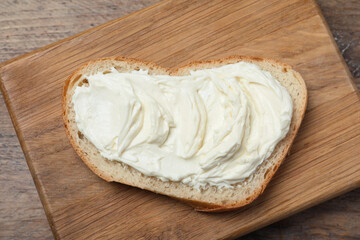 Slice of bread with tasty cream cheese on wooden table, top view