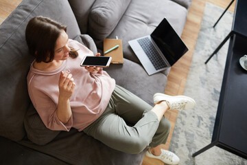 Young woman sitting on sofa with laptop and talking on mobile phone, she working at home