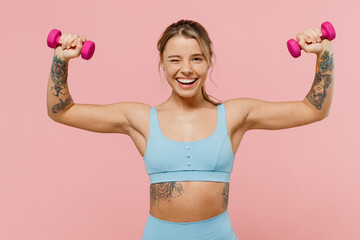 Young happy strong sporty athletic fitness trainer instructor woman wear blue tracksuit spend time in home gym hold female dumbbells isolated on pastel plain pink background. Workout sport concept.