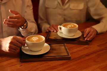Fototapeta na wymiar Couple with cups of aromatic coffee at wooden table, closeup