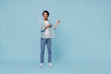 Full size body length happy young black curly man 20s wear white shirt pointing index fingers aside on workspace area copy space mock up isolated on plain pastel light blue background studio portrait