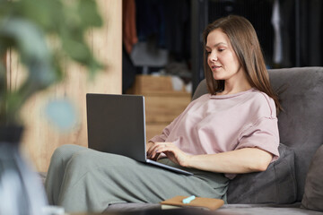 Young woman sitting on sofa and typing on laptop, she working online at home