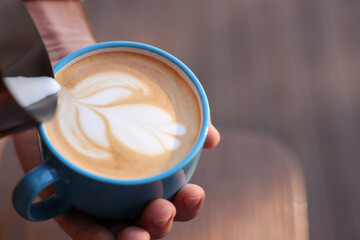 Barista pouring milk into cup of coffee on blurred background, closeup. Space for text