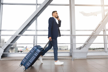Handsome middle-eastern man walking with suitcase and talking on cellphone in airport