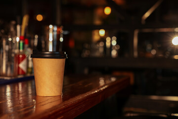 Paper coffee cup on wooden table in cafe. Space for text