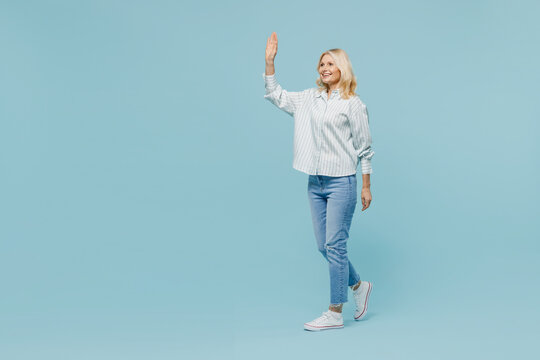 Full Body Elderly Fun Woman 50s Wear Casual Striped Shirt Looking Camera Walk Go Strolling Waving Hand Isolated On Plain Pastel Light Blue Color Background Studio Portrait. People Lifestyle Concept.