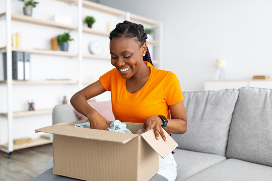 Online Delivery Service. Cheerful African American Woman Unpacking Parcel Box With Purchase At Home