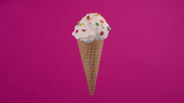 Yummy ice cream in waffle cone. Sweet dessert decorated with colorful sprinkles, rotating soft cream, gelato icecream scoop over pink background