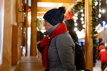 Obraz na płótnie Canvas caucasian woman wearing hat and red scarf buying treats in kiosk at christmas market