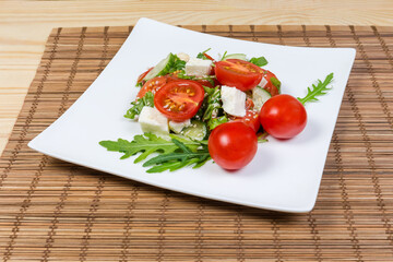 Salad with fresh cherry tomatoes, mozzarella and greens close-up