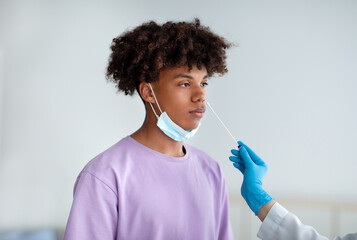 Covid diagnostic and testing. Doctor making nasal coronavirus PCR test for black teenager, using swab stick at clinic