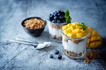 Mango  and blueberry Greek yogurt granola parfait in a glass